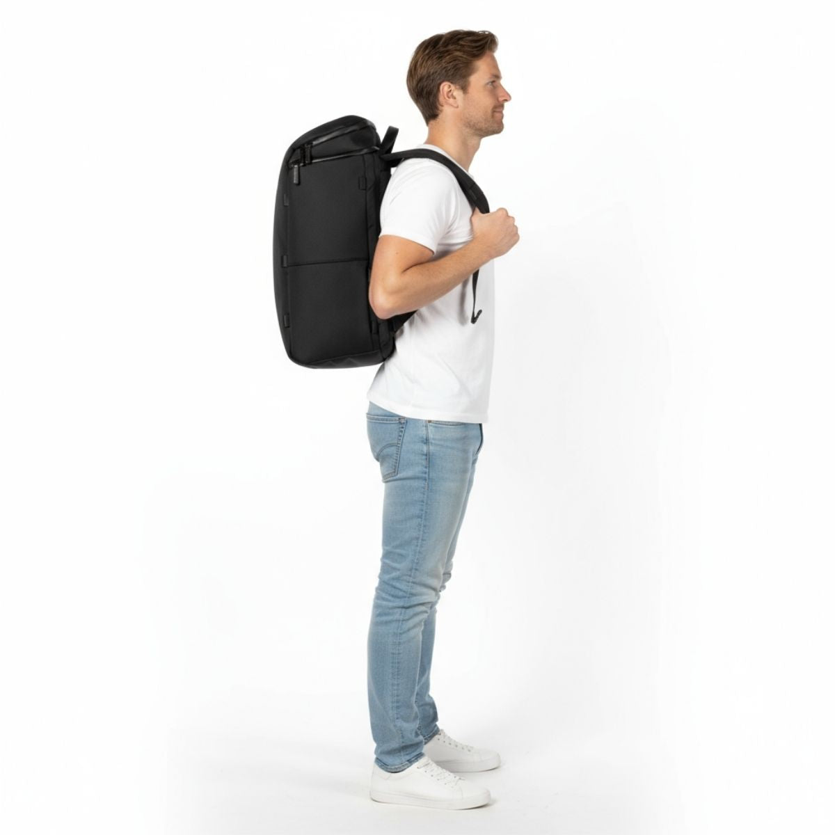 Man in wit T-shirt en jeans draagt een zwarte Zeeksack-rugzak, van opzij gezien.