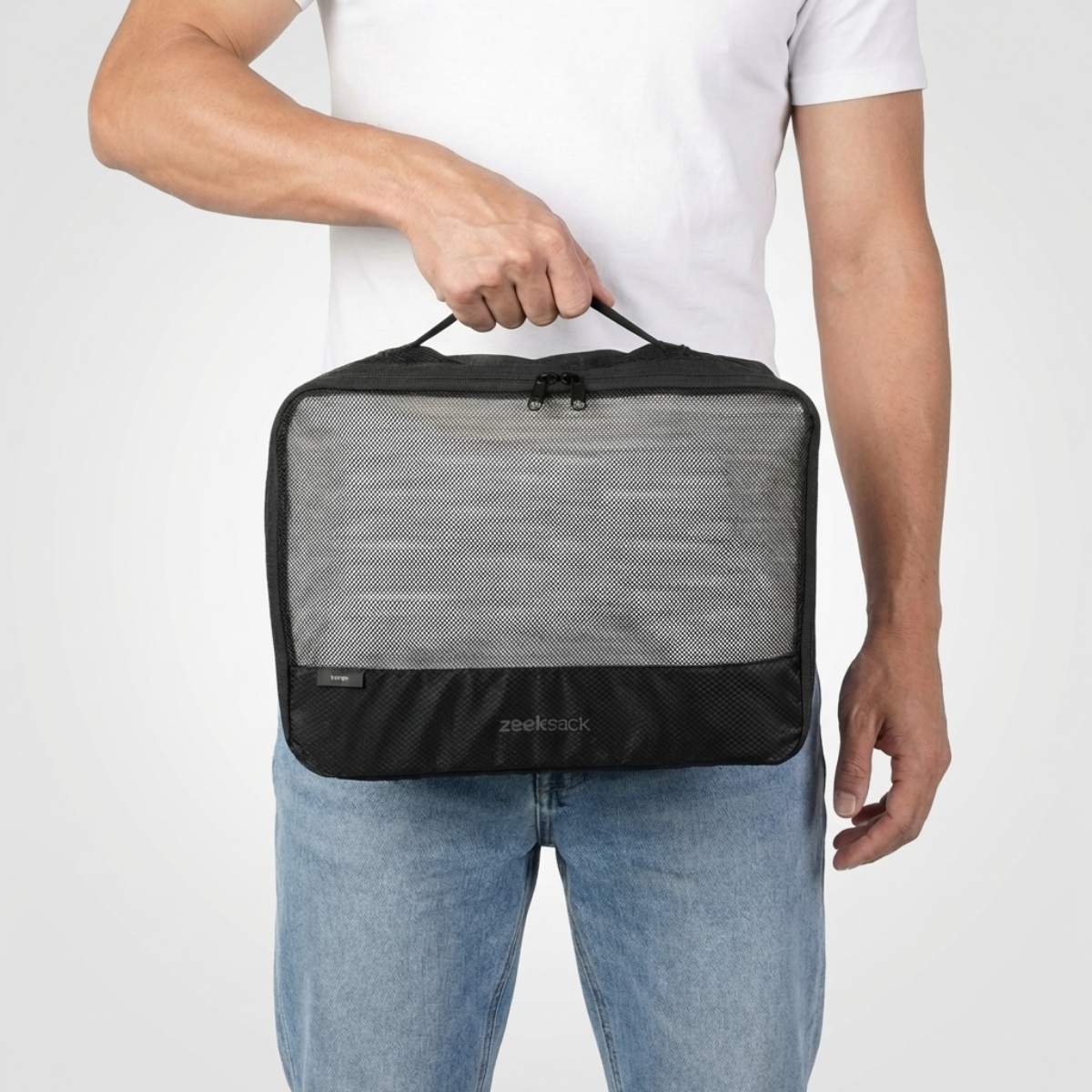 Man in wit T-shirt en jeans houdt een grote zwarte packing cube met meshvak aan de voorkant.