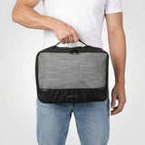 Man in wit T-shirt en jeans houdt een grote zwarte packing cube met meshvak aan de voorkant.