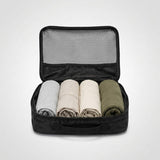 Geopende zwarte packing cube met vier opgerolde kledingstukken erin en een meshvak in het deksel.