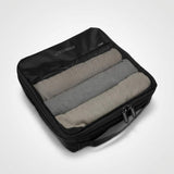 Zwarte packing cube met deksel van mesh, gevuld met drie opgerolde kledingstukken.