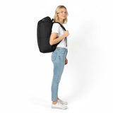 Vrouw in wit T-shirt en jeans met een zwarte Zeeksack-rugzak, van opzij gezien.